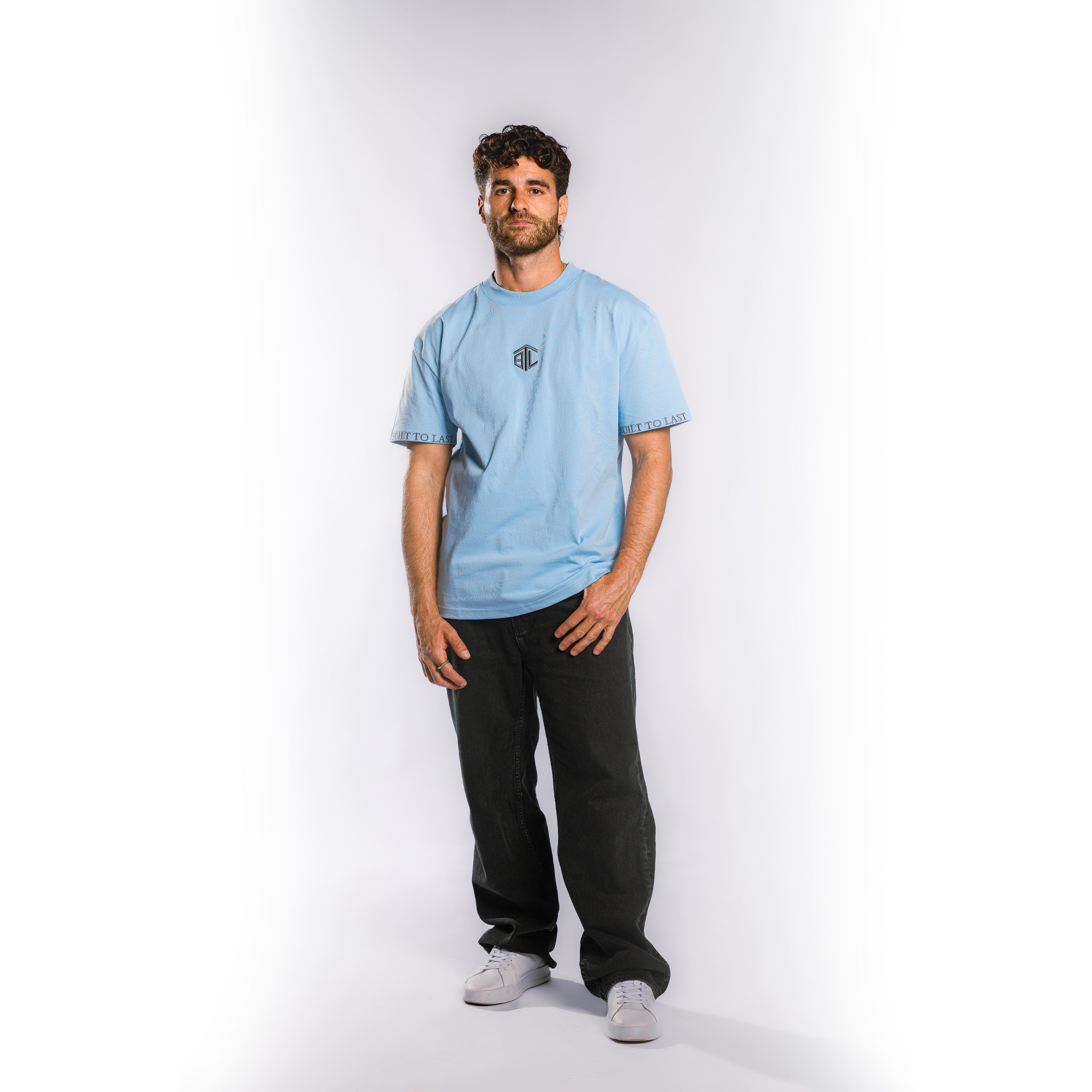 Front view of model wearing Built to Last Monolith Tee Blue heavyweight cotton T-shirt with embroidered chest logo and branded sleeve detail
