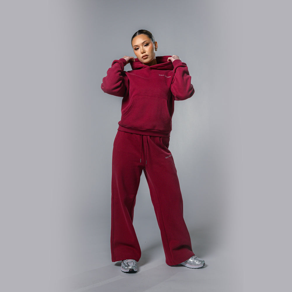 Model adjusting hood of women's burgundy relaxed fit tracksuit set by Built To Last.