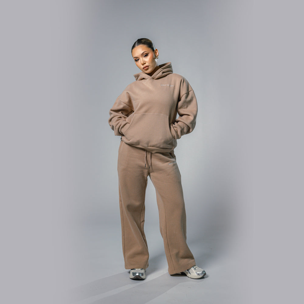 Model with hands in pocket of women's beige relaxed fit tracksuit set by Built To Last.