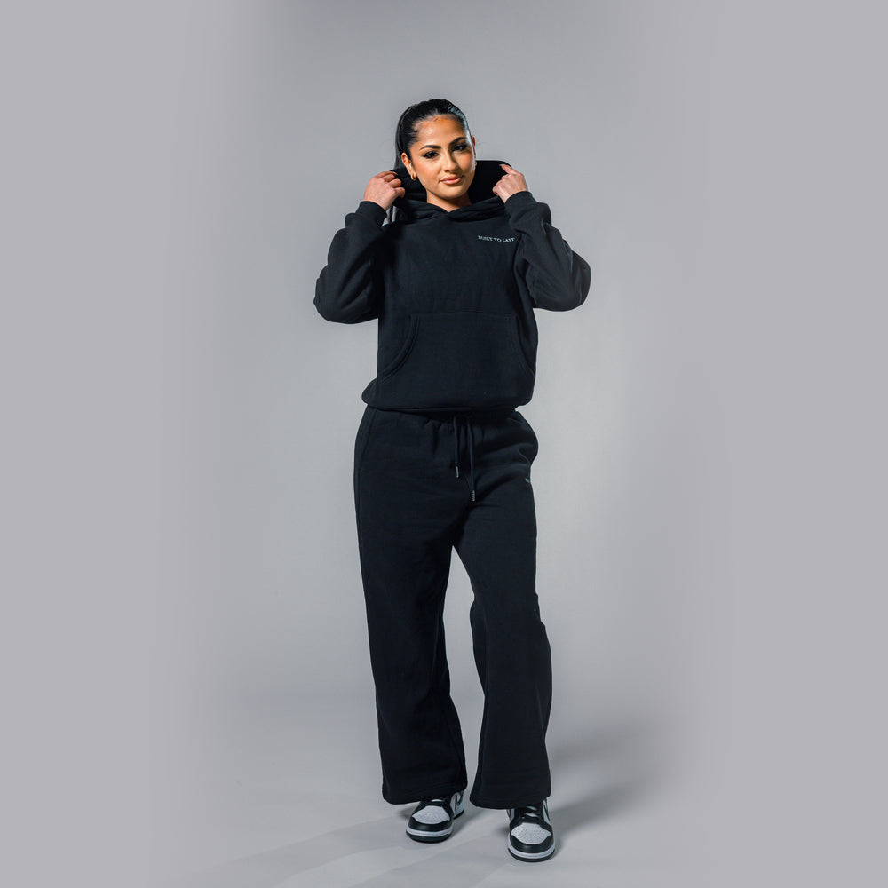 Model adjusting hood of women's black relaxed fit tracksuit set by Built To Last.