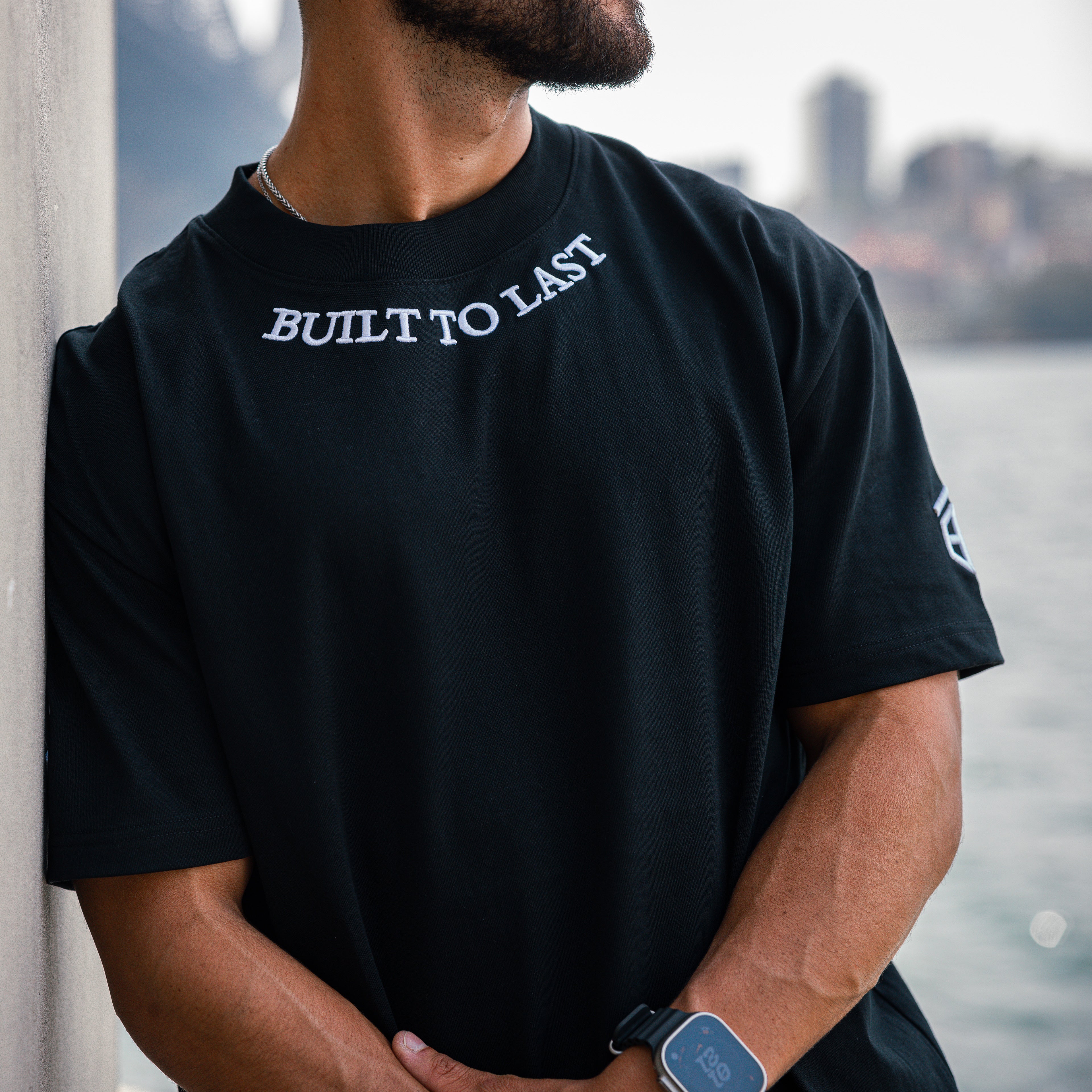 Close-up of model wearing Built to Last Legacy Tee Black heavyweight cotton T-shirt with embroidered neckline logo