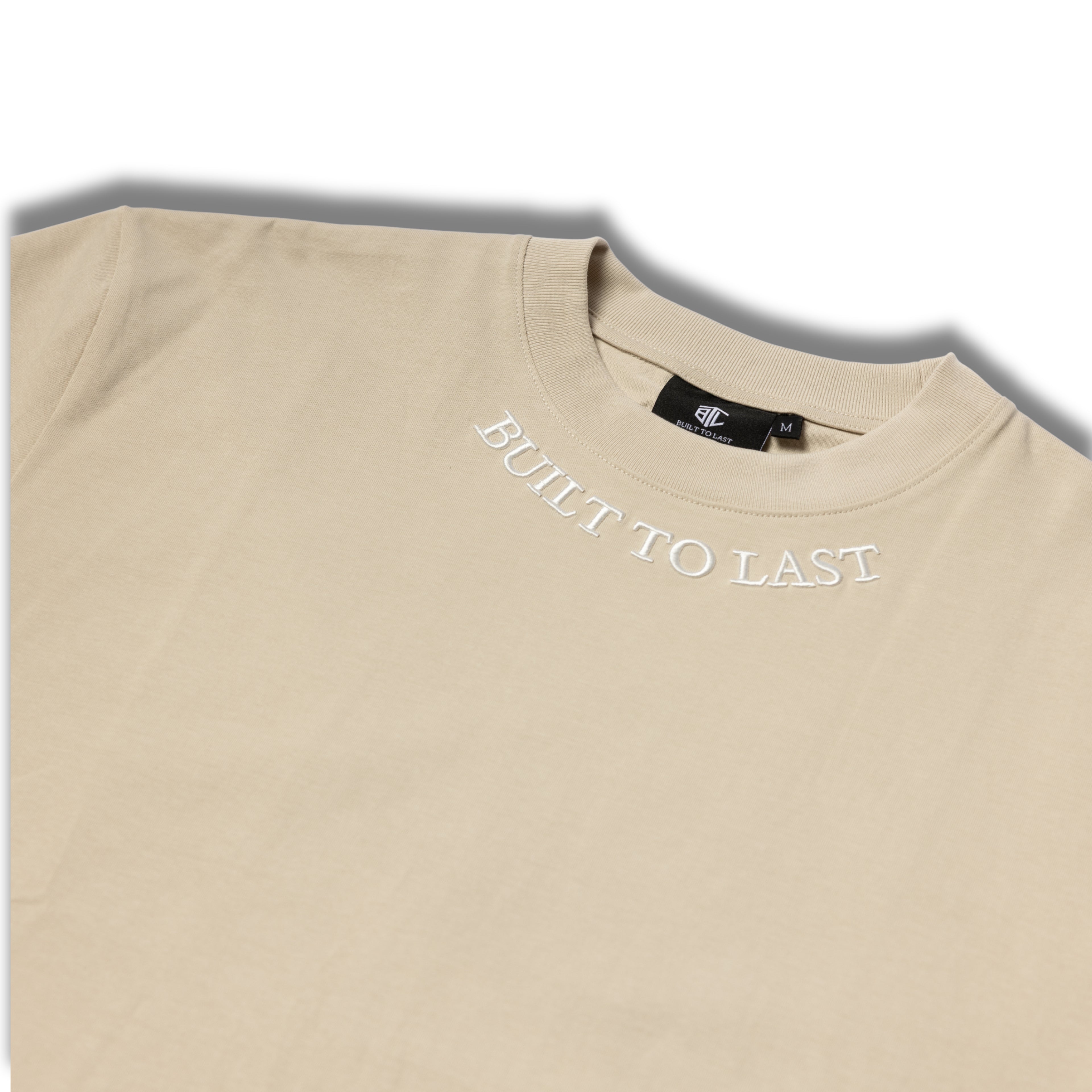 Close-up of Built to Last Legacy Tee Champagne embroidered neckline logo on premium heavyweight cotton T-shirt