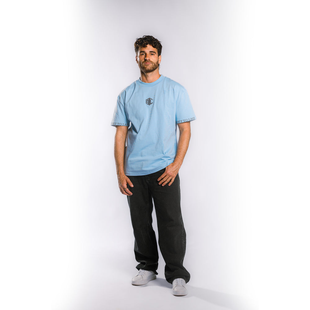 Front view of model wearing Built to Last Monolith Tee Blue heavyweight cotton T-shirt with embroidered chest logo and branded sleeve detail