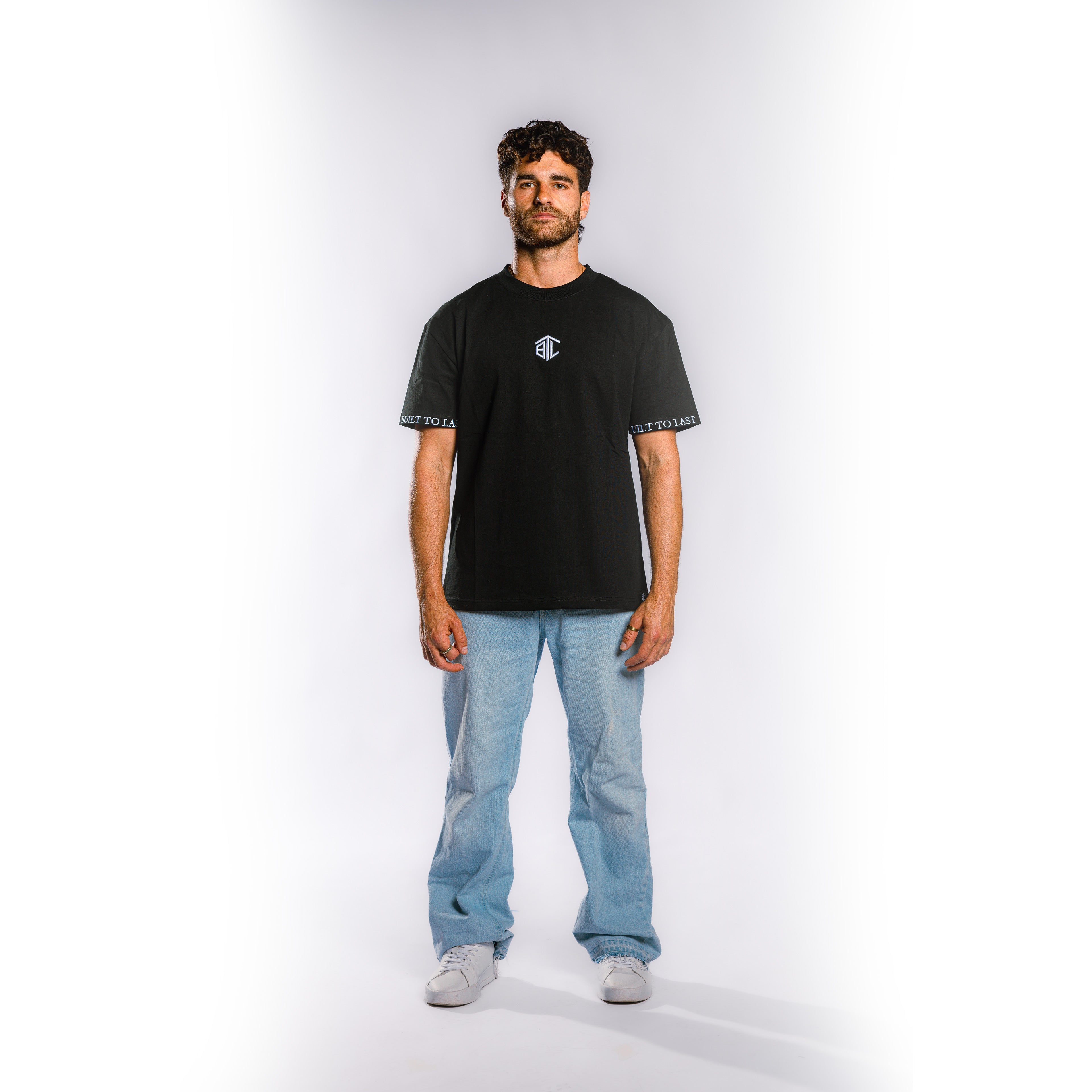 Front view of model wearing Built to Last Monolith Tee Black heavyweight cotton T-shirt with embroidered chest logo and branded sleeve detail