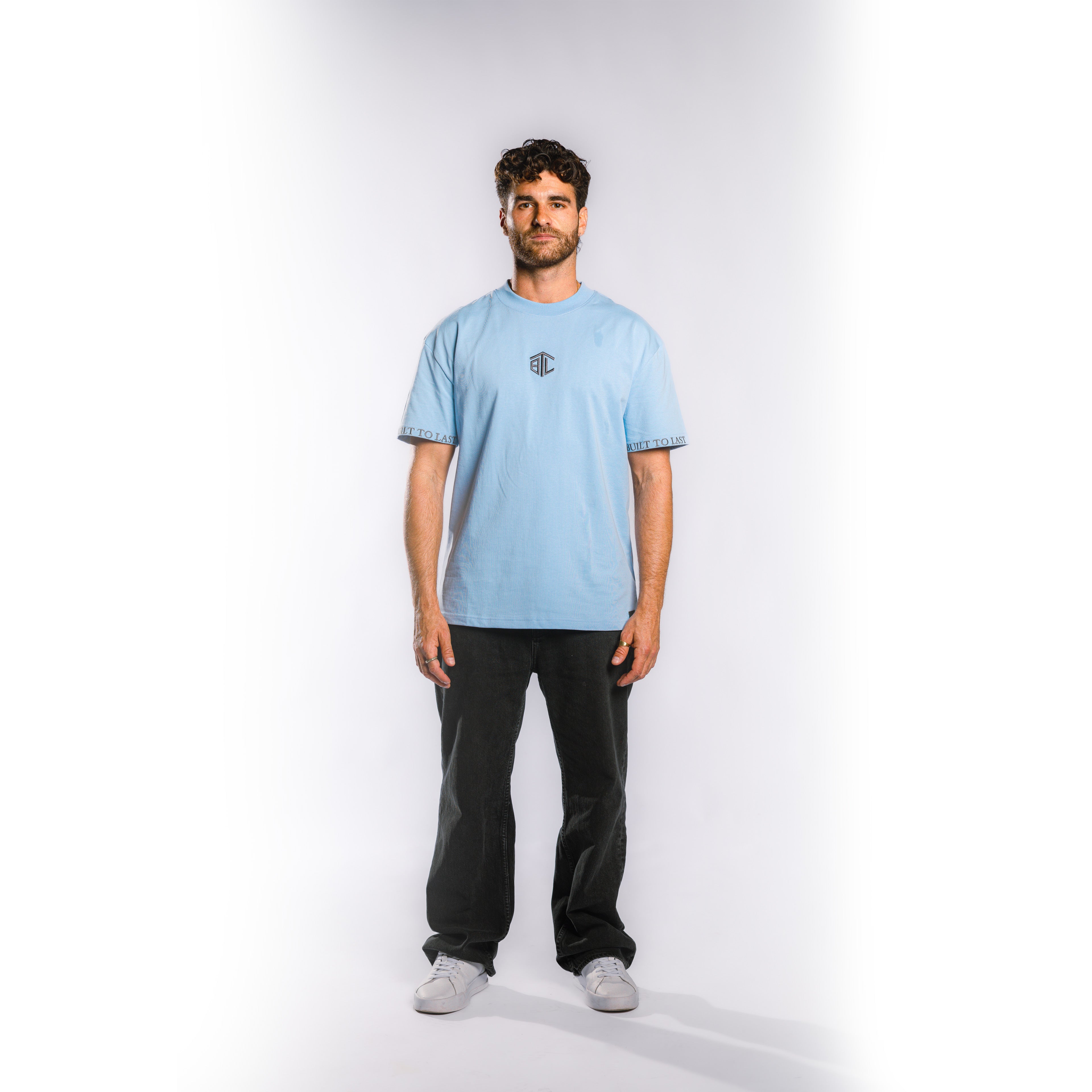 Front view of model wearing Built to Last Monolith Tee Blue heavyweight cotton T-shirt with embroidered chest logo and branded sleeve detail