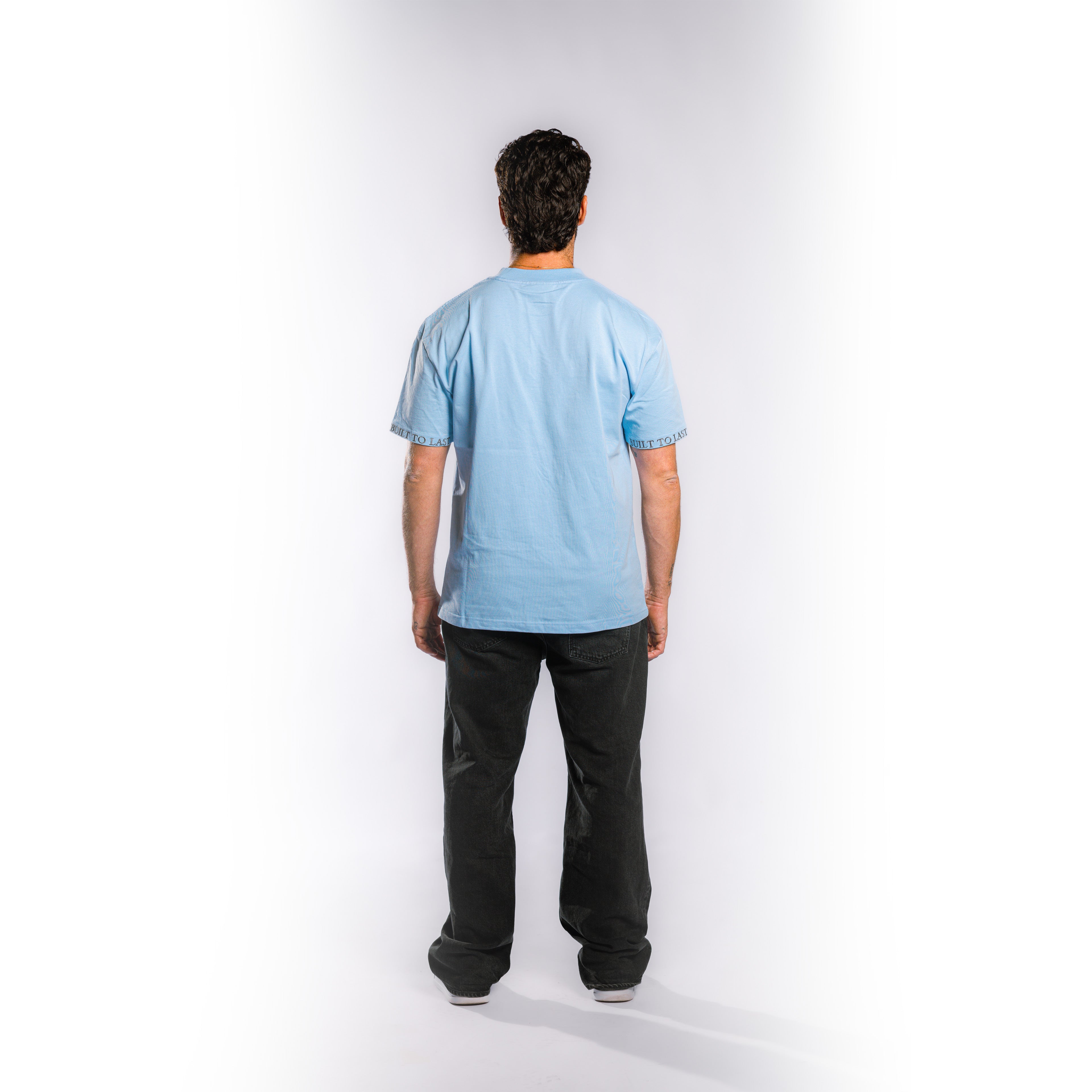 Back view of model wearing Built to Last Monolith Tee Blue heavyweight cotton T-shirt with branded sleeve detail